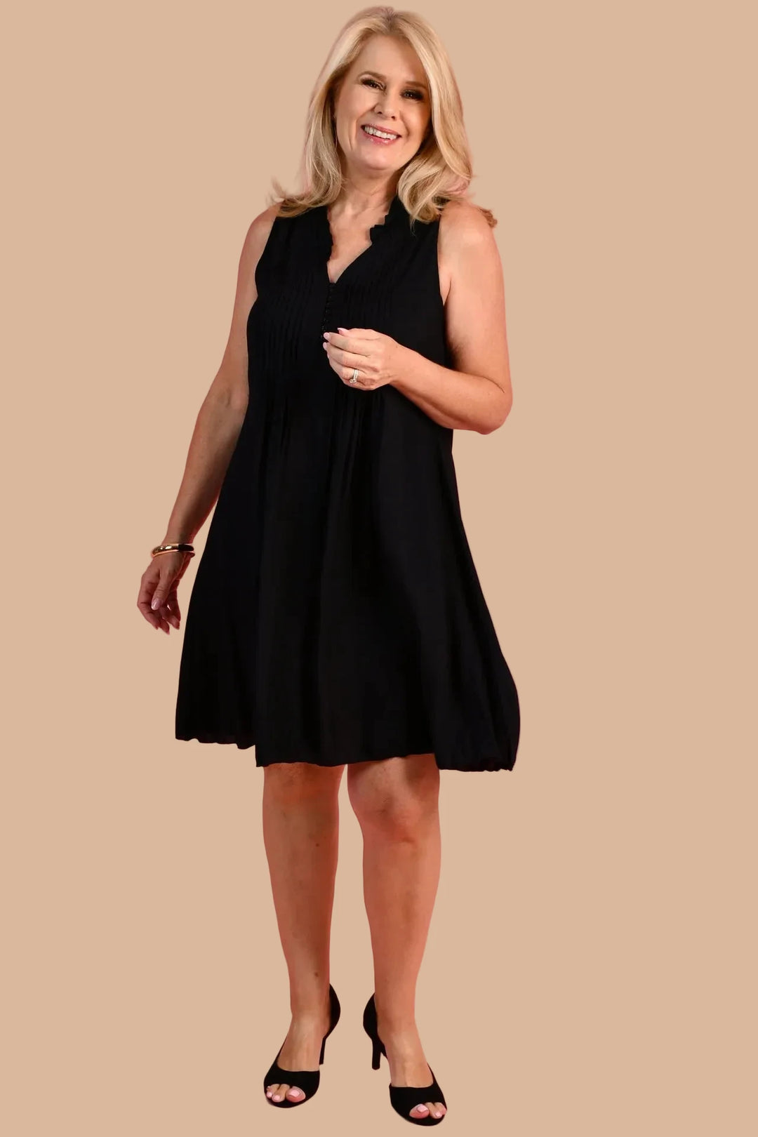Woman wearing a black sleeveless dress against a pink background