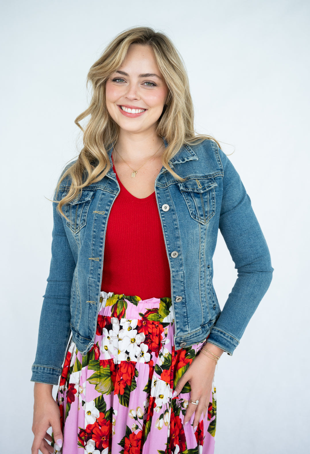 Woman wearing a denim jacket, red top, and floral skirt on a white background