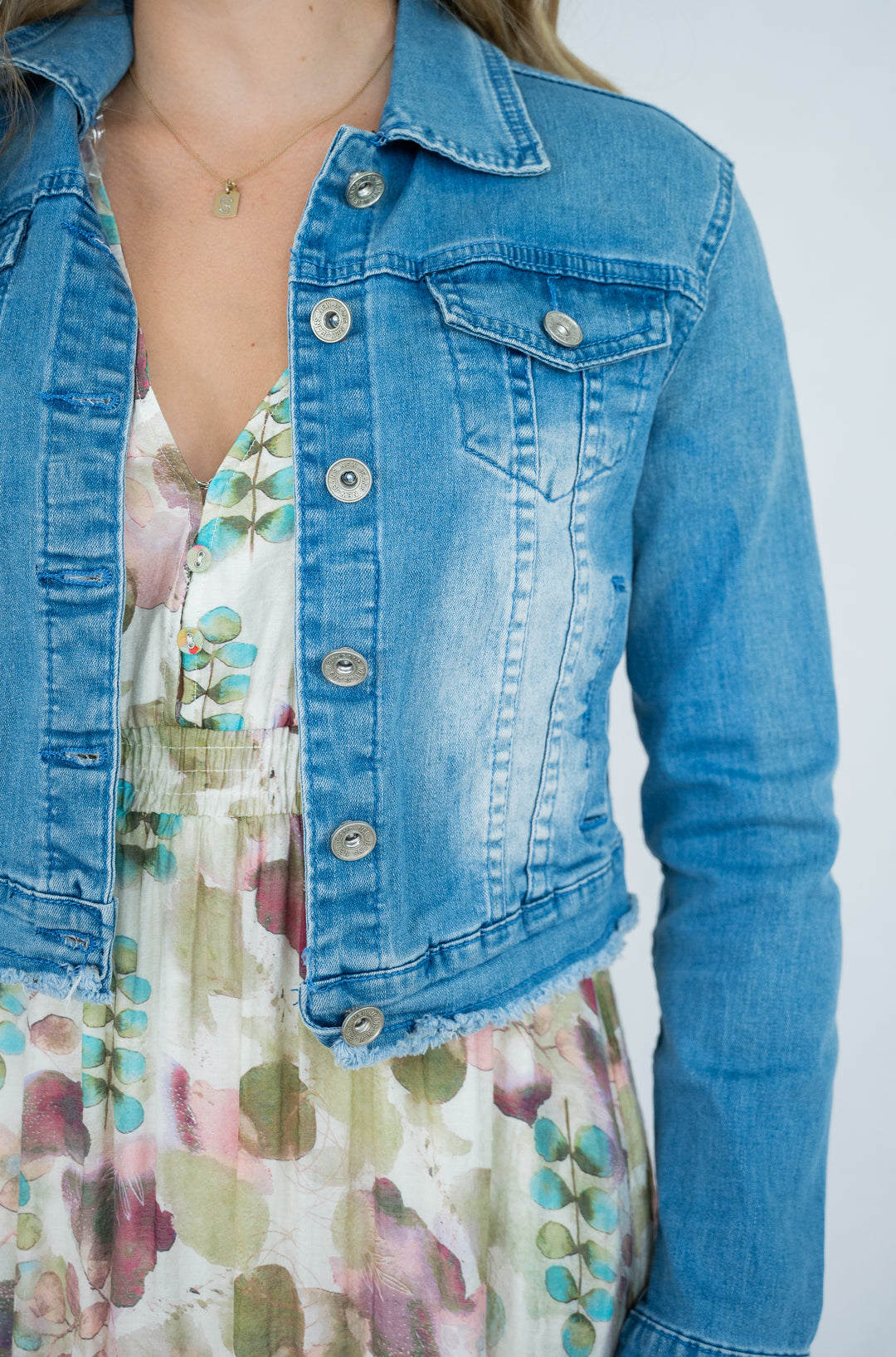 Person wearing a blue denim jacket over a floral dress on a white background
