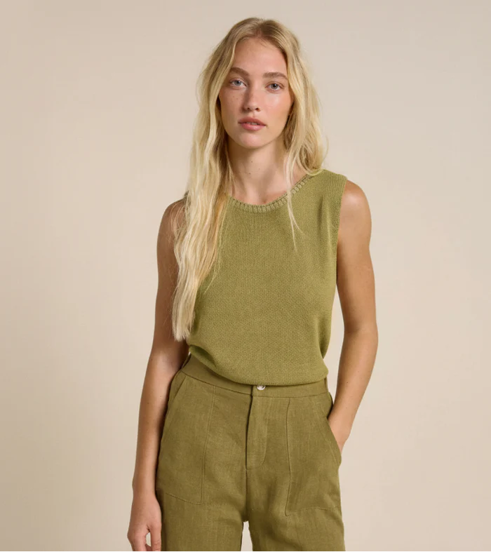 Woman wearing a green sleeveless top and pants against a beige background