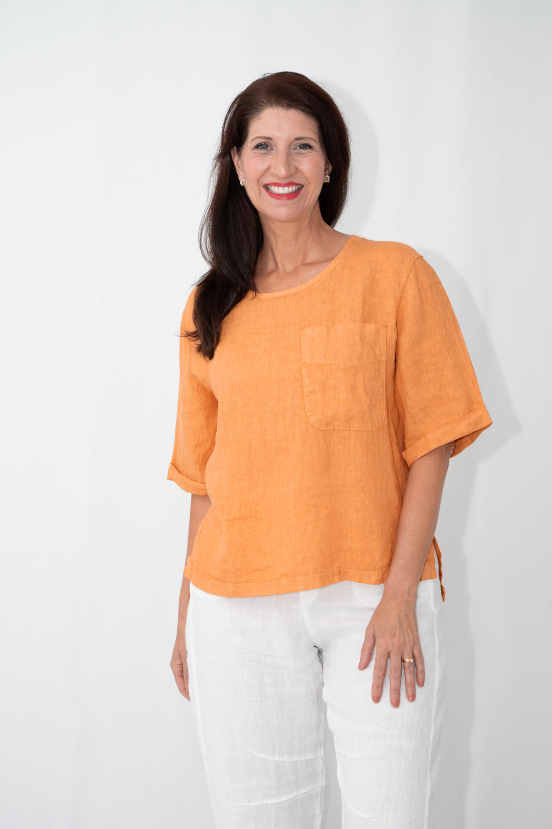 Woman wearing an orange top and white pants against a white background