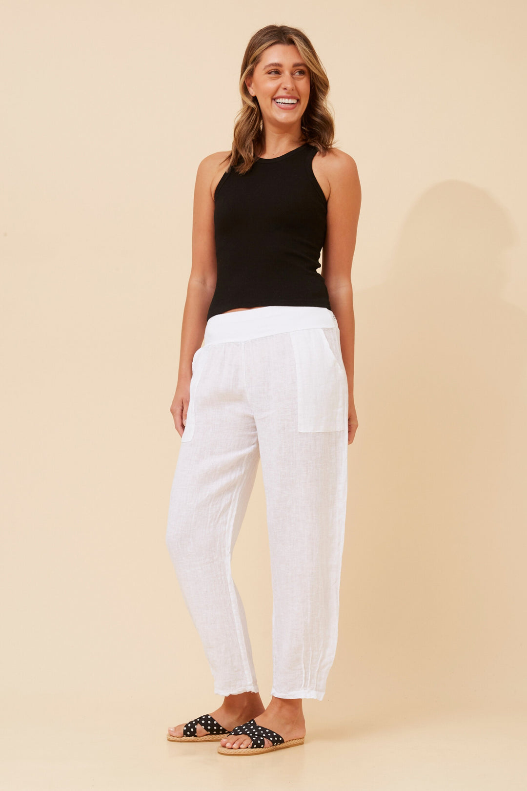 Woman wearing a black sleeveless top and white pants on a beige background